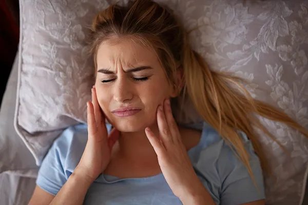 Pained woman suffering from bruxism and rubbing her jaw while in bed