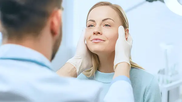 Cosmetic surgeon examines a woman's face, inspecting her healed face after plastic surgery with amazing results.