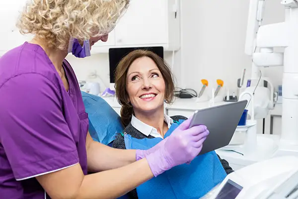 A female dental patient in the dental chair, with a dentist next to her holding a tablet and showing her dental information.
